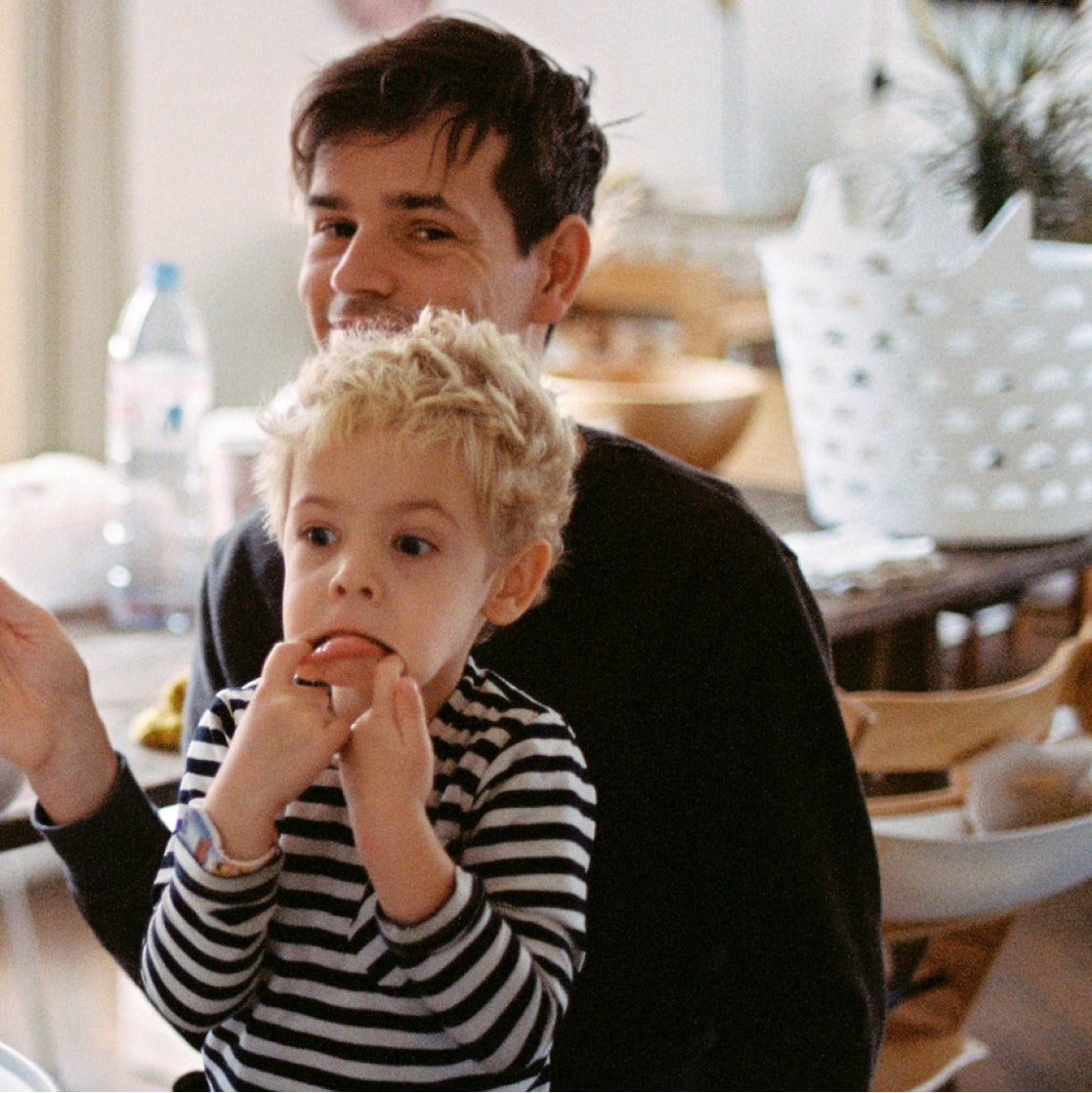 A young man holding a child on his lap on a white chair in an indoor setting.