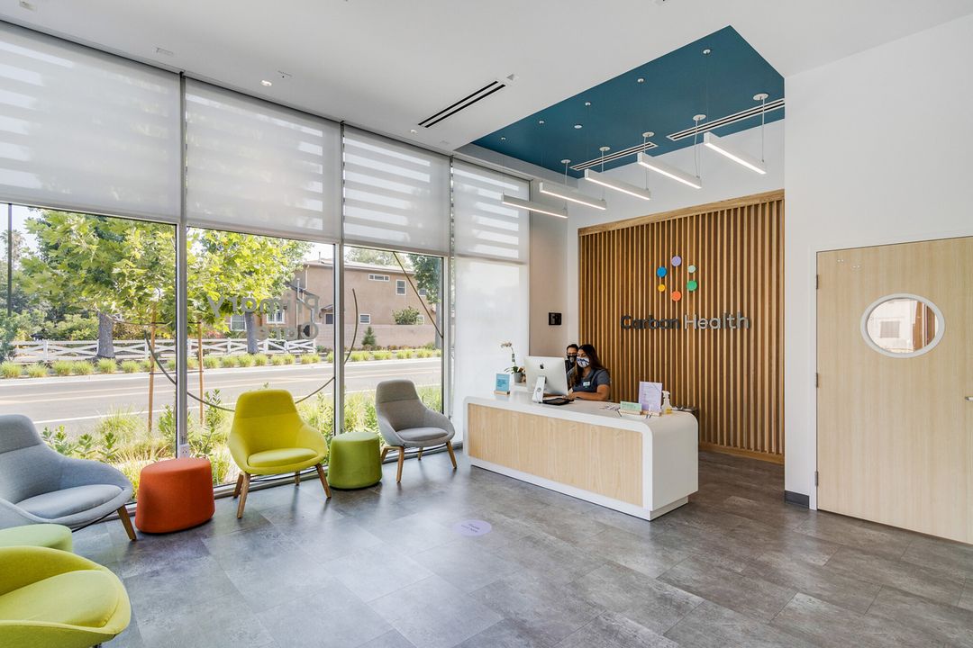 A woman working at a reception desk in a room with a modern and sleek interior design and large windows that let in natural light
