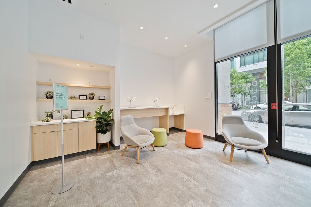 A spacious and modern indoor room features a large window, a desk, a small desk and two chairs