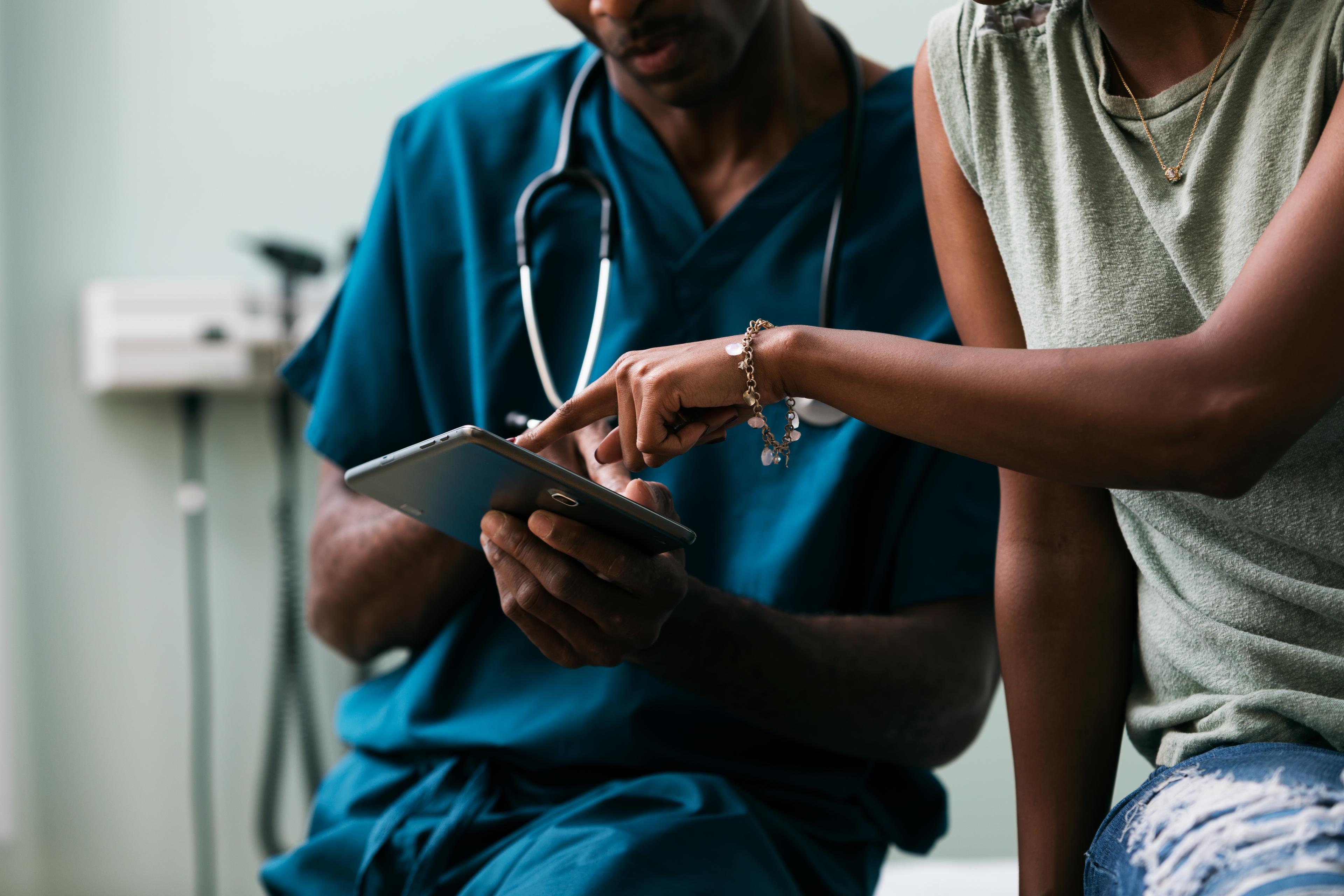 Healthcare provider reviewing tablet with patient in exam room
